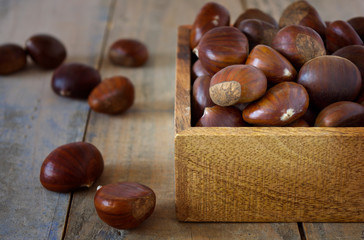 WOODEN BOX FILLED WITH RAW CHESTNUTS ON DARK BACKGROUND HORIZONTAL