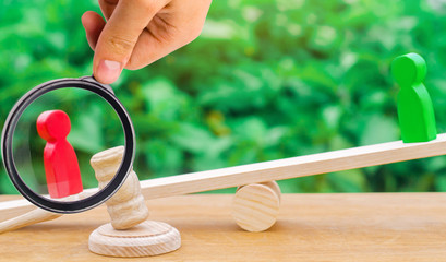 wooden figures of people. rivals in business stand on the scales. trial. conflict. victory and...