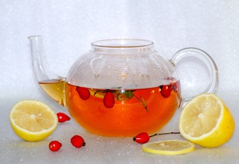 Hot rosehip tea with lemon in a glass teapot, nearby is rosehip and lemon slices