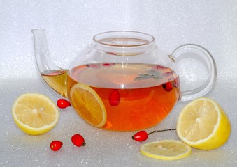 Hot rosehip tea with lemon in a glass teapot, nearby is rosehip and lemon slices