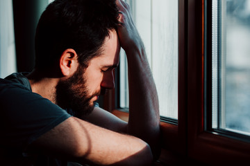 Bearded young man by the window in despair 