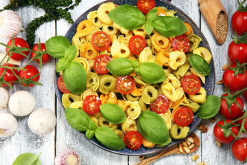 pasta. tricolor tortellini pasta salad with tomatoes and onions on wood table background.
