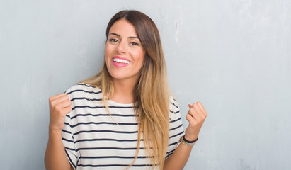 Fototapeta premium Young adult woman over grunge grey wall wearing navy t-shirt celebrating surprised and amazed for success with arms raised and open eyes. Winner concept.