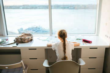 Portrait of cute happy kid girl at home making homework, indoors, view from the back