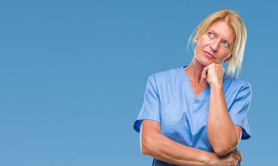 Middle age blonde woman wearing doctor nurse uniform over isolated background with hand on chin thinking about question, pensive expression. Smiling with thoughtful face. Doubt concept.