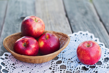 Autumn harvest. Red ripe apples in a wicker basket on a knitted napkin on a table in the garden on a Sunny day. Rustic style	