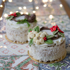 White New Year or Christmas cake decorated with cream poinsettia flowers, pine cones, cottons and spruce twigs on a colorful table. A birthday cake for those born in winter.Copy space, selective focus