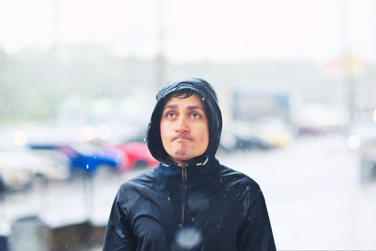 Portrait Of A Young Man In A Jacket With A Hood In The Rain On Blurred Background City Street, Close-up.