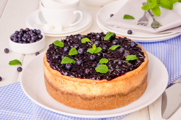 Delicious cream cheesecake with lemon zest and blueberry jam on a plate on a white wooden background