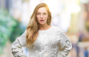 Fototapeta premium Young beautiful blonde woman wearing winter sweater and sunglasses over isolated background afraid and shocked with surprise expression, fear and excited face.