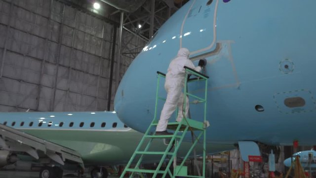 Painting the aircraft at the factory. The engineer repairing the aircraft. Maintenance of passenger aircraft. Repair of an aircraft wing. Passenger plane in the hangar in the repair. 4K
