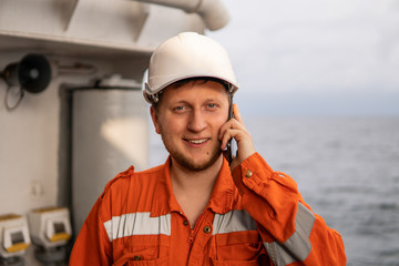 Marine Deck Officer or seaman on deck of vessel or ship . He is speaking on the mobile cell phone