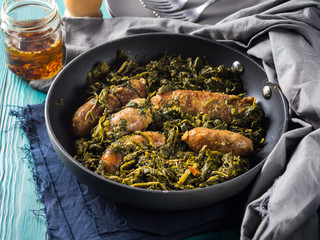 Italian sausages with rapini broccoli in a skillet with table setting on green wooden table