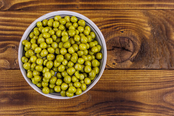 Bowl with canned green peas  on wooden table. Top view