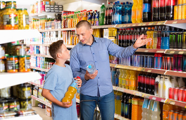 Smiling father friendly discussing with preteen boy while choosing beverages in food store
