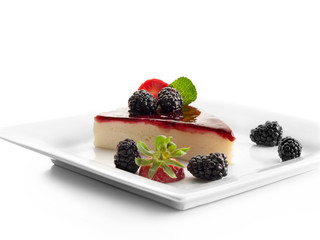 Trozo de tarta de queso decorado con fresas y frambuesas negras sobre un fondo blanco