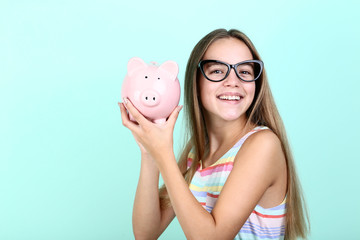 Young girl holding pink piggybank on mint background