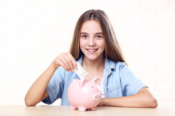Young girl with pink piggybank and dollar banknote sitting at table
