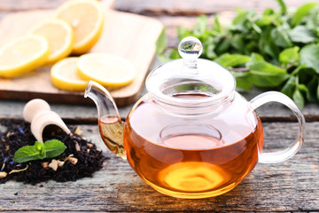 Glass teapot with mint leafs and sliced lemons on wooden table