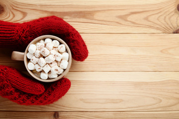 Cappuccino with marshmallows in hands on brown wooden table
