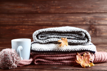 Folded sweaters, scarf with cup and maple leafs on wooden background