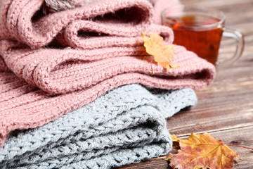 Stack of knitted scarfs with cup of tea on wooden table