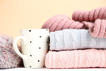 Obraz na płótnie Canvas Stack of folded sweaters with cup and scarf on beige background