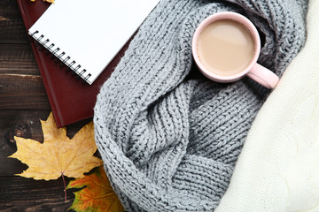 Knitted scarf and sweater with cup of coffee on wooden table