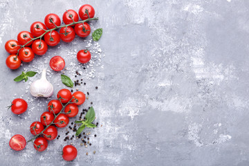 Cherry tomatoes with basil leafs, garlic and spices on grey wooden table