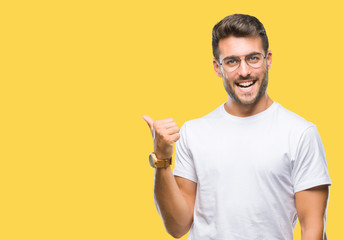 Young handsome man wearing glasses over isolated background smiling with happy face looking and pointing to the side with thumb up.