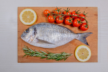 Fresh dorado fish with cherry tomatoes, rosemary and lemon on wooden cutting board