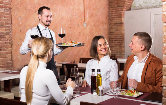 smiling waiter placing order in front of guests