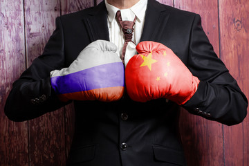 Businessman in boxing gloves with Russian and China flag. Russia versus China concept.