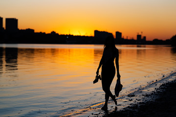 girl walking barefoot along the river at dawn holding shoes in her hands and traveling