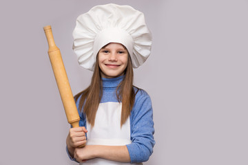 Children cook. Happy little girl in chef uniform holds rolling pin isolated on white background.