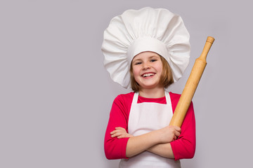 Children cook. Happy little girl in chef uniform holds rolling pin isolated on white background.