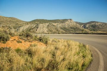 Curved small narrow empty car road in highland scenic mountain landscape in warm dry summer weather