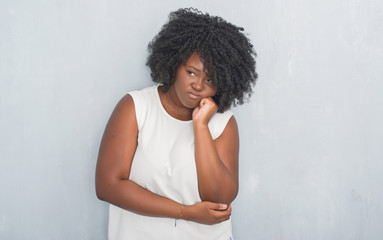 Young african american woman over grey grunge wall thinking looking tired and bored with depression problems with crossed arms.