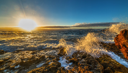 Rough sea by Sardinia rocky shore at sunset