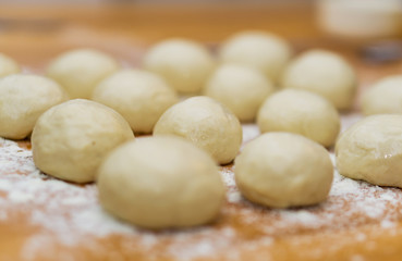 Fototapeta na wymiar A close-up of small, white balls of home-made dough for a multi-layered banitsa and pizza on a kitchen table, flour for kneading. Shallow depth of focus.