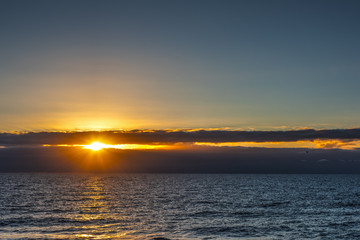 Sun shining through dark clouds over the sea at sunset