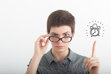 Young strict irritated business woman in glasses pointing index finger up on drawn alarm clock on the white background. Time is running out. Lady boss. Achievement career wealth concept. Copy space