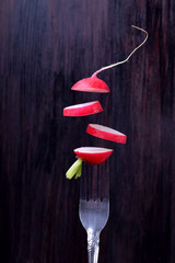 Pieces of fresh radish on the fork and are flying against the dark background