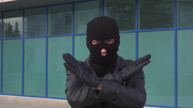 Criminal man thief or robber in mask is showing stop sign gesture by crossing his hands.