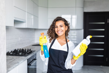 Young latin woman with bottle of detergent in kitchen