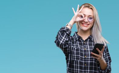 Obraz premium Young blonde woman texting sending message using smartphone over isolated background with happy face smiling doing ok sign with hand on eye looking through fingers