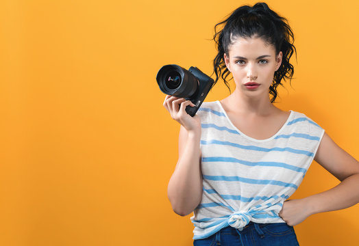 Young woman with a professional digital SLR camera on a yellow background