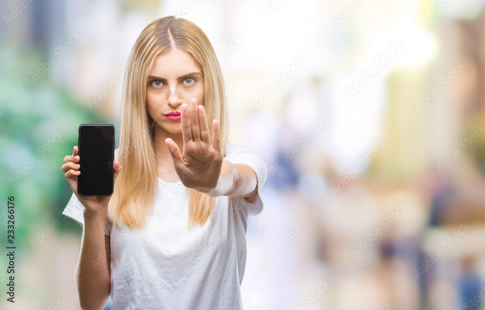 Sticker Young beautiful blonde woman showing smartphone over isolated background with open hand doing stop sign with serious and confident expression, defense gesture