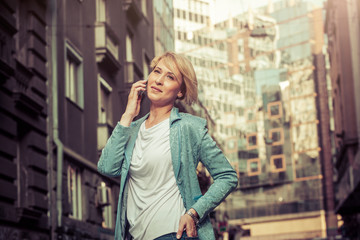 Fototapeta premium Confident mid-age woman talking on a cell phone in the street