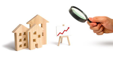 Magnifying glass is looking at the Wooden houses stand with red arrow up. Growing demand for housing and real estate. The growth of the city and its population. Investments. concept of rising prices